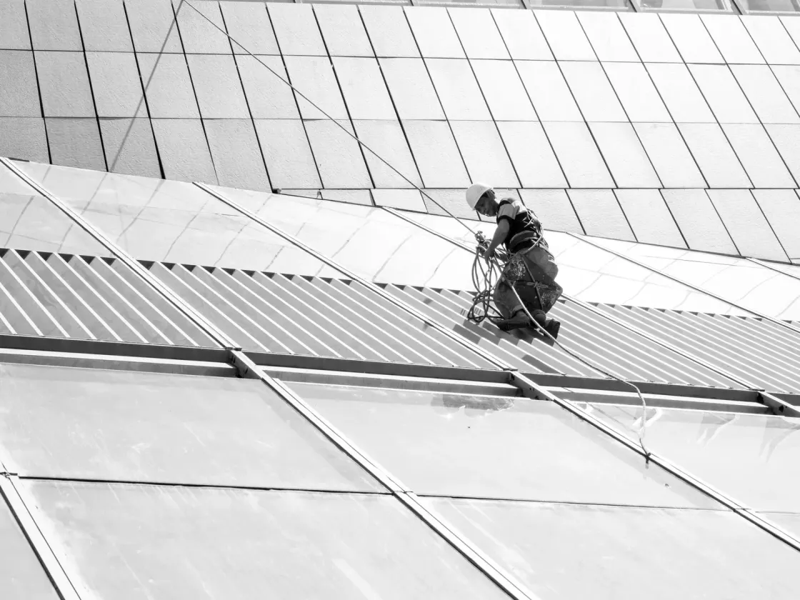 Vakman met helm en harnas werkt gezekerd aan een gebouwgevel